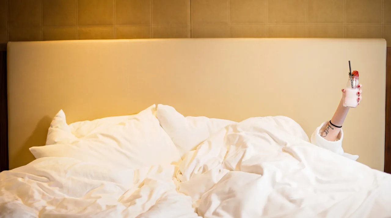 Yumuşak ışıklı beyaz otel yatağında selfie çeken misafir